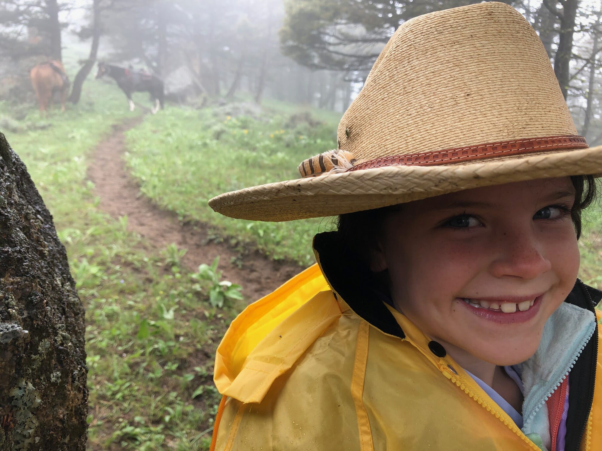 A little girl wearing a cowboy hat smiles amid a Montana rain storm.