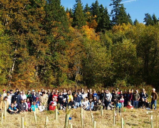 A group of volunteers poses behind newly planted trees.