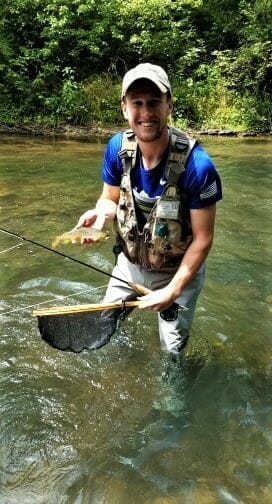 An angler poses with a small brown trout on the Battenkill River.