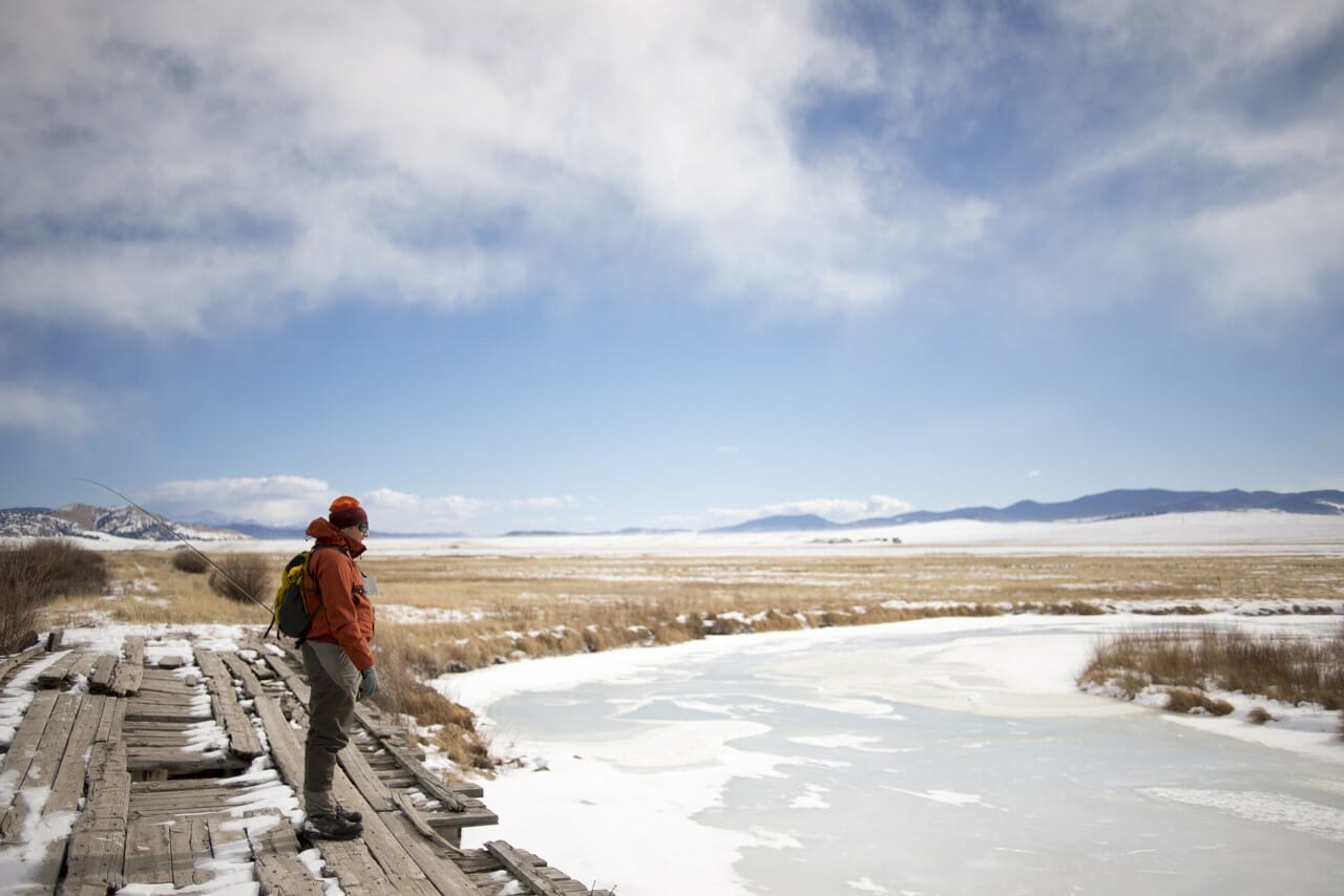 An angler stands over a frozen creek.