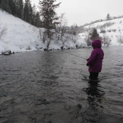 A girl fly fishes in the winter.