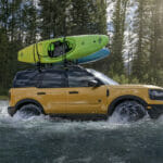 A Ford Bronco drives through a river.
