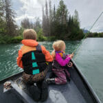 two young children sitting in the front of the boat fishing