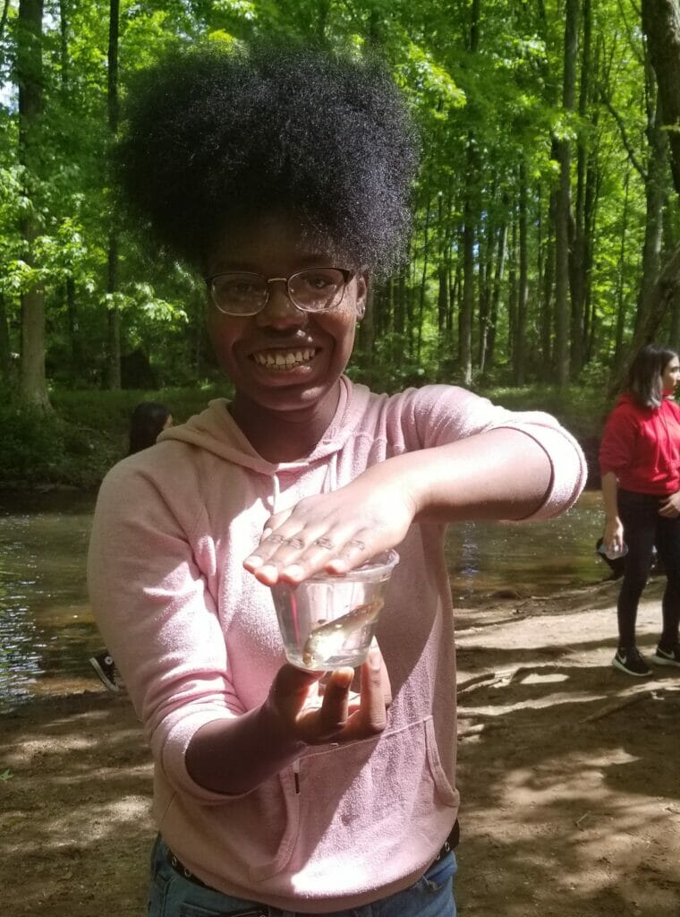 Teen girl with a small trout in a cup of water