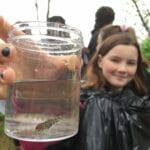 Young girl with small trout in glass of water