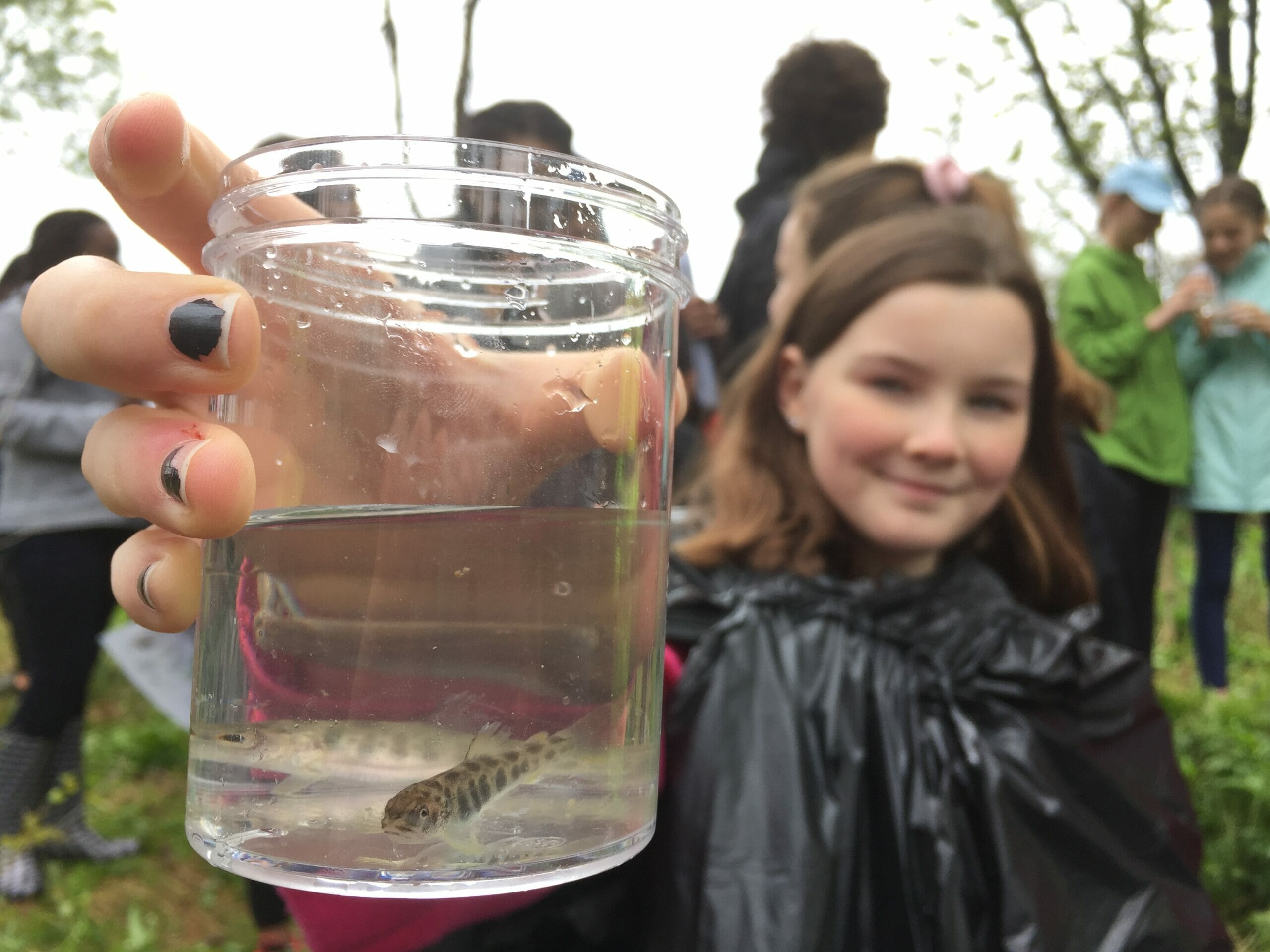 Young girl with small trout in glass of water