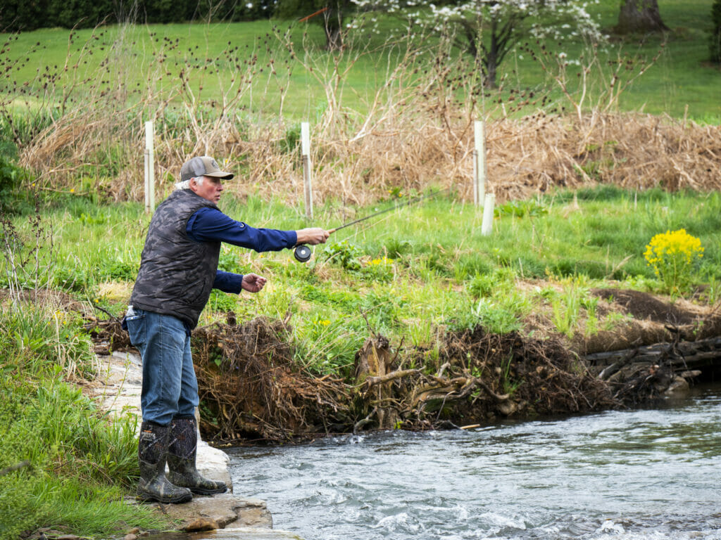 Man stands on rocky bank casting into river