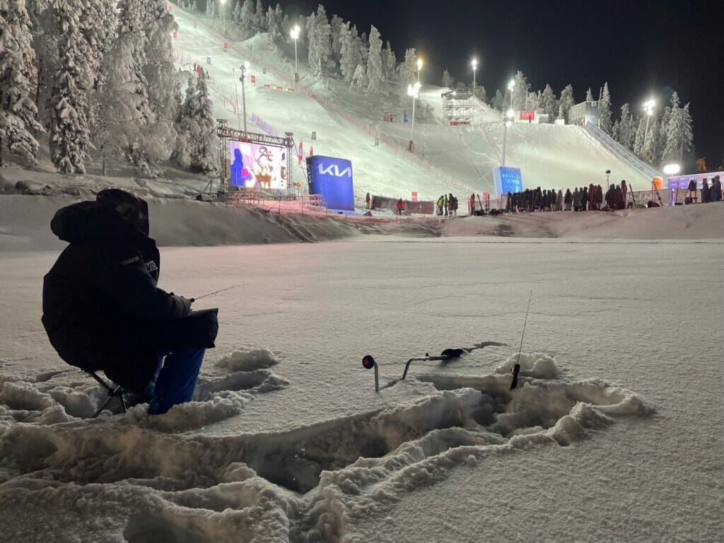 Silhouette of Olympian Eric Loughran, seated, ice fishing in front of ski run