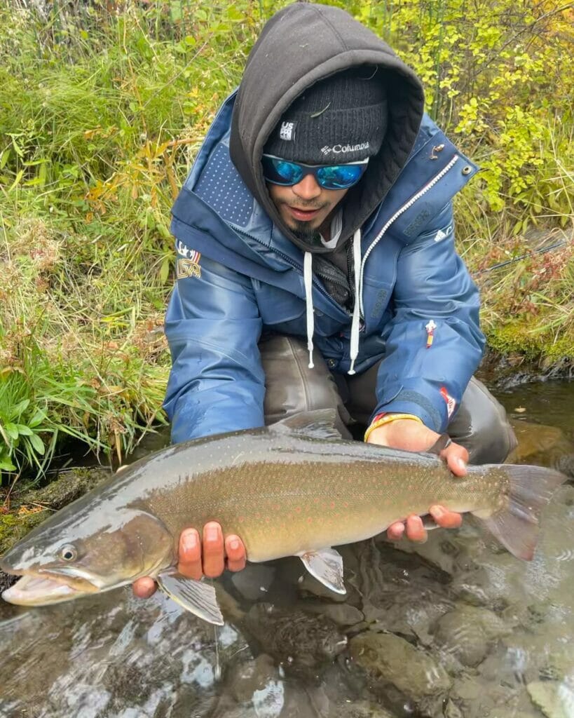 Eric crouched in a river, holding a large trout
