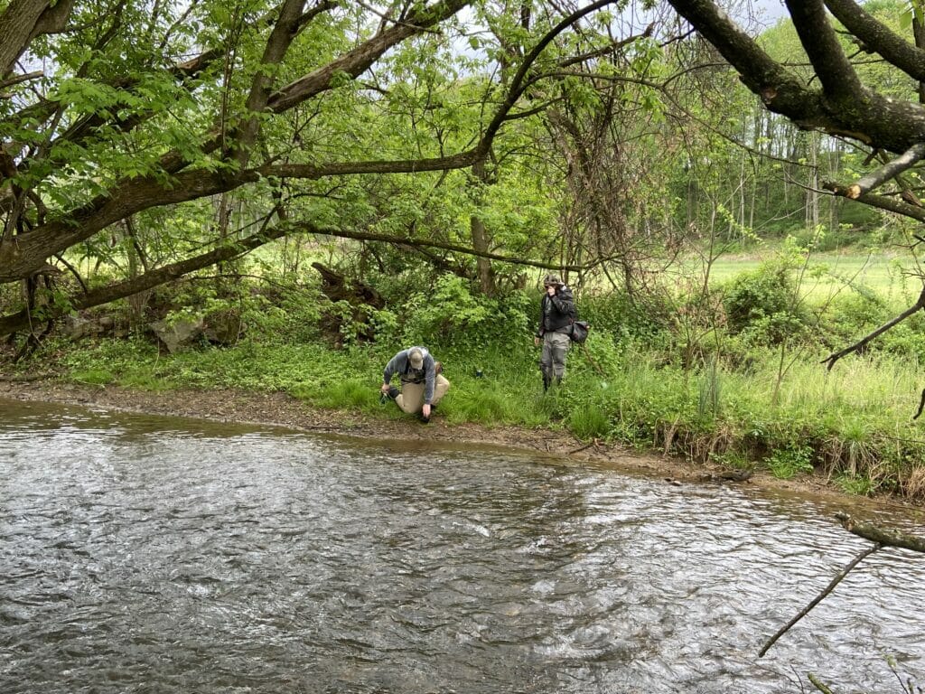 Man kneels down next to stream messing with his equipment