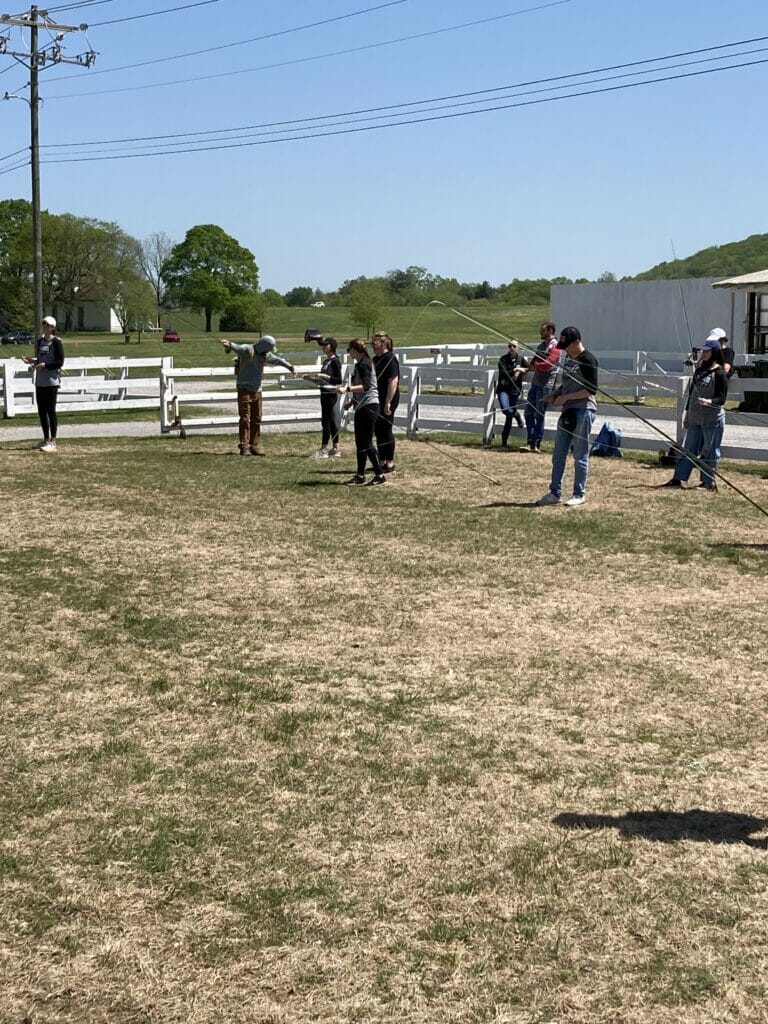 A group of people practice fly casting in a field