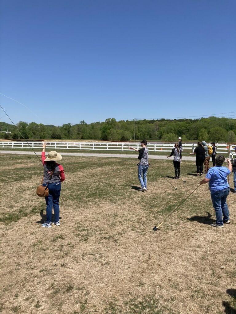 View from behind of people practice fly casting in a field