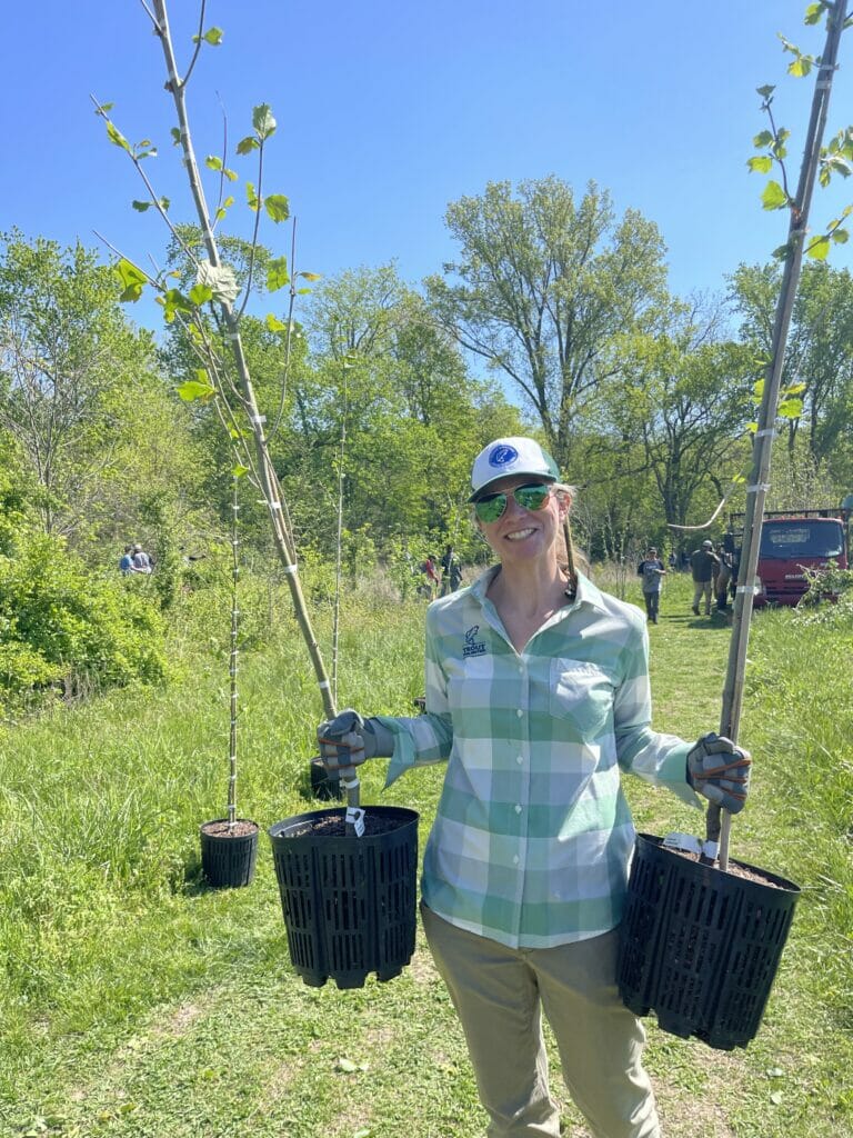 A smiling woman carries two potted trees