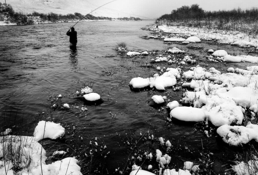 Black and white image of man in a winter river casting