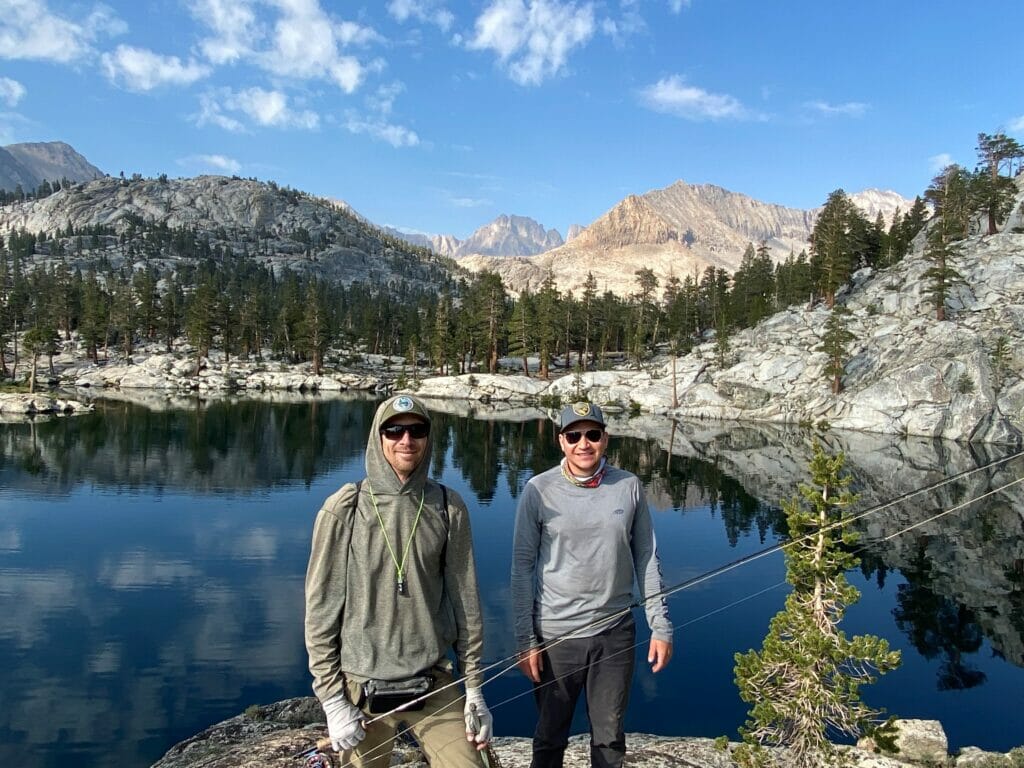 Two men with rods standing in front of mountains and lake