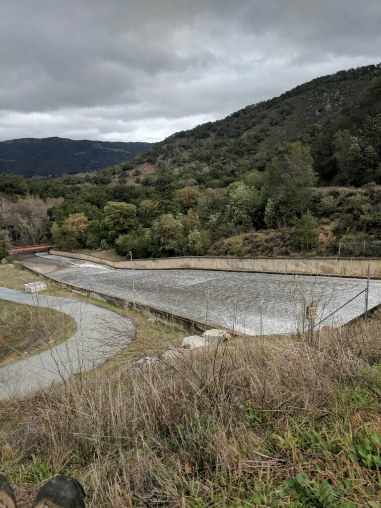 Water runs downhill on damn spillway with hills in background
