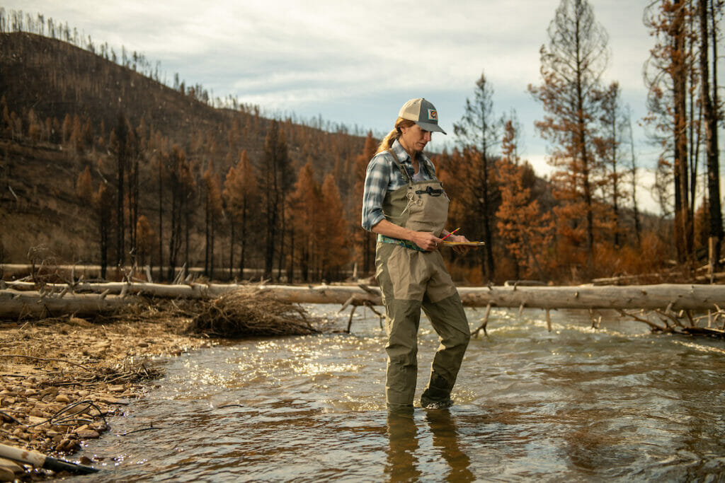 Woman waders standing in river with pencil and clip board