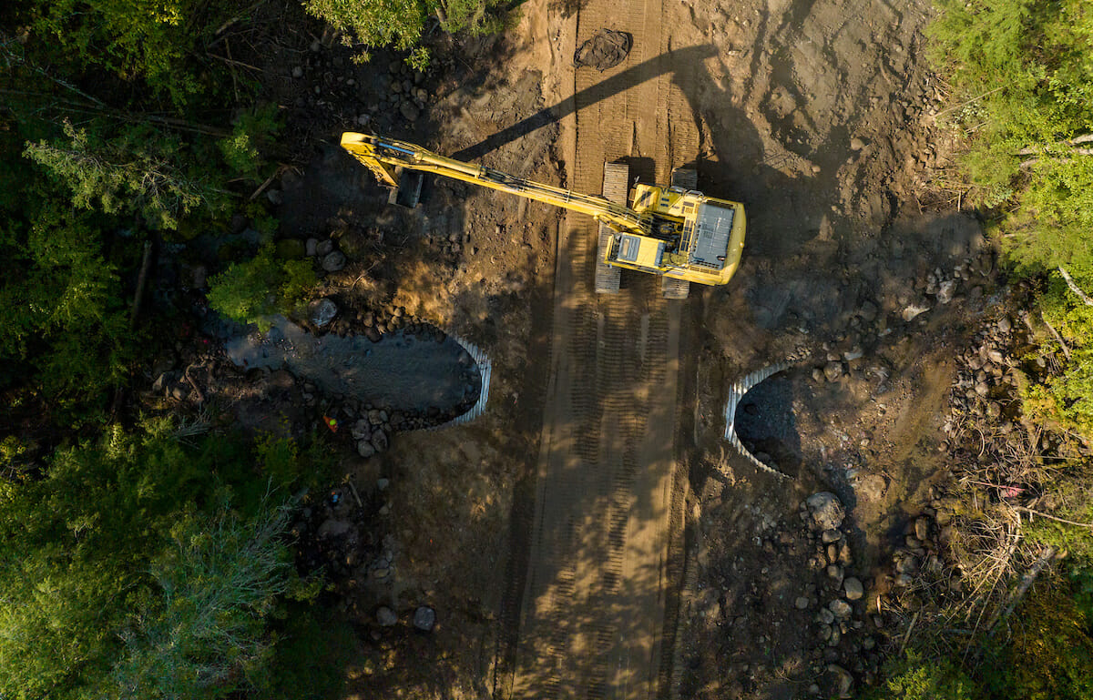 Backhoe next to a culvert on a dirt road