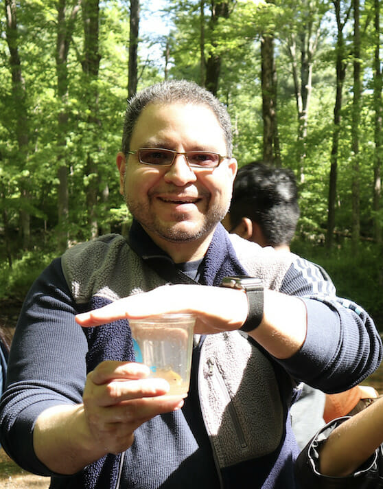Smiling Ricardo Nieves holds a trout in a cup of water that he prepares to release