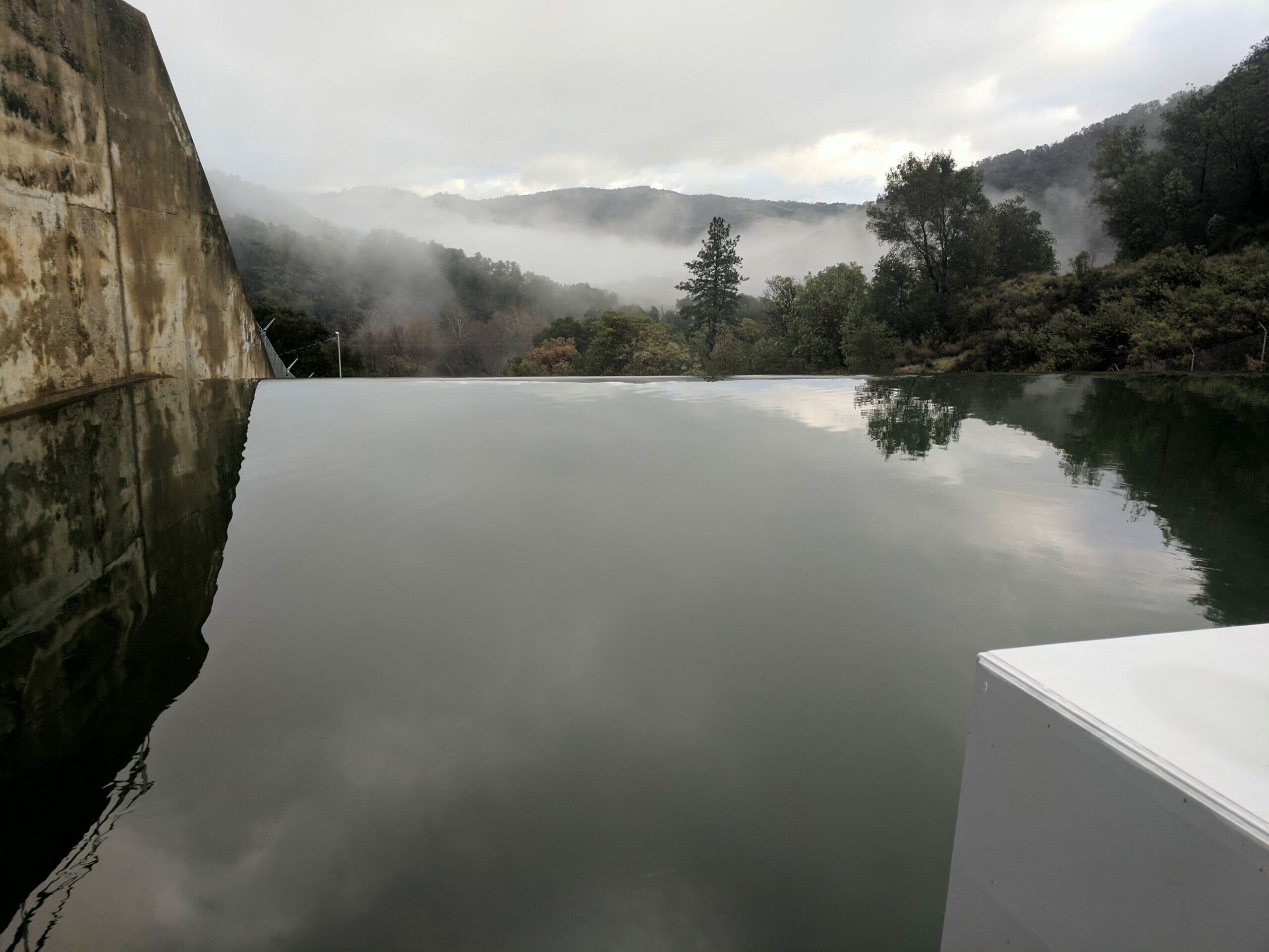 Smooth, still water next to damn with misty mountains in background