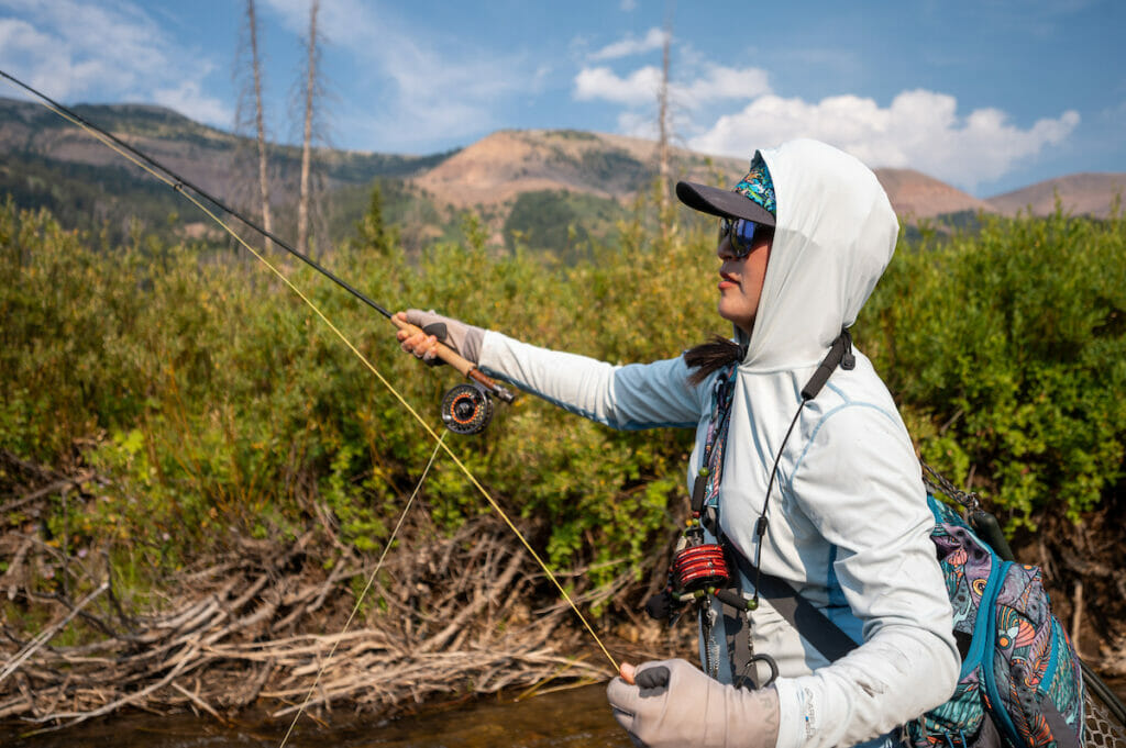 Person in sunglasses and hoodie uses fly fishing rod to cast