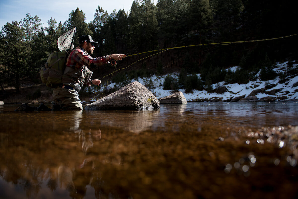 Seen from water level, man stands in river and casts