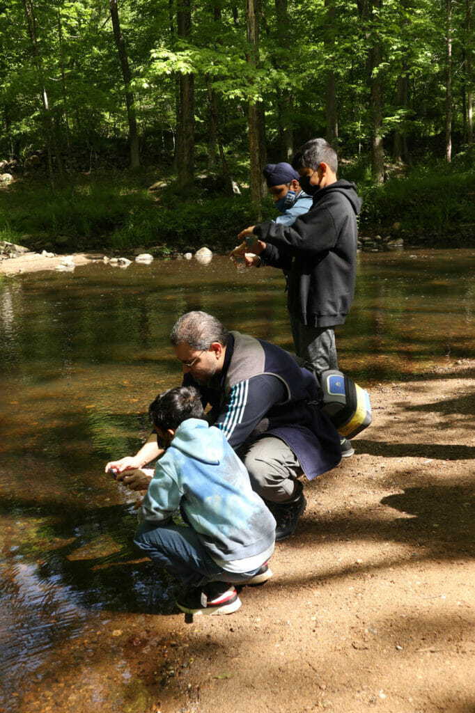 Teacher helps elementary students release fish into a stream, for some reason