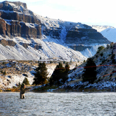 Person in wide river casting with snowy mountains behind