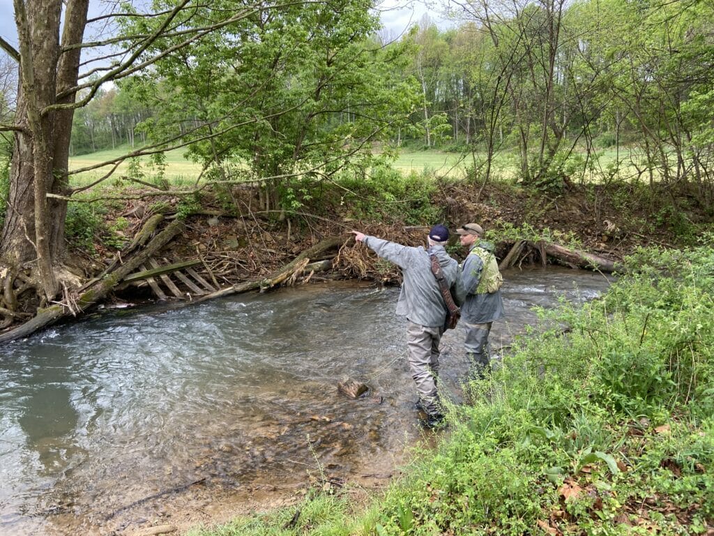 Man points across stream while talking to younger man