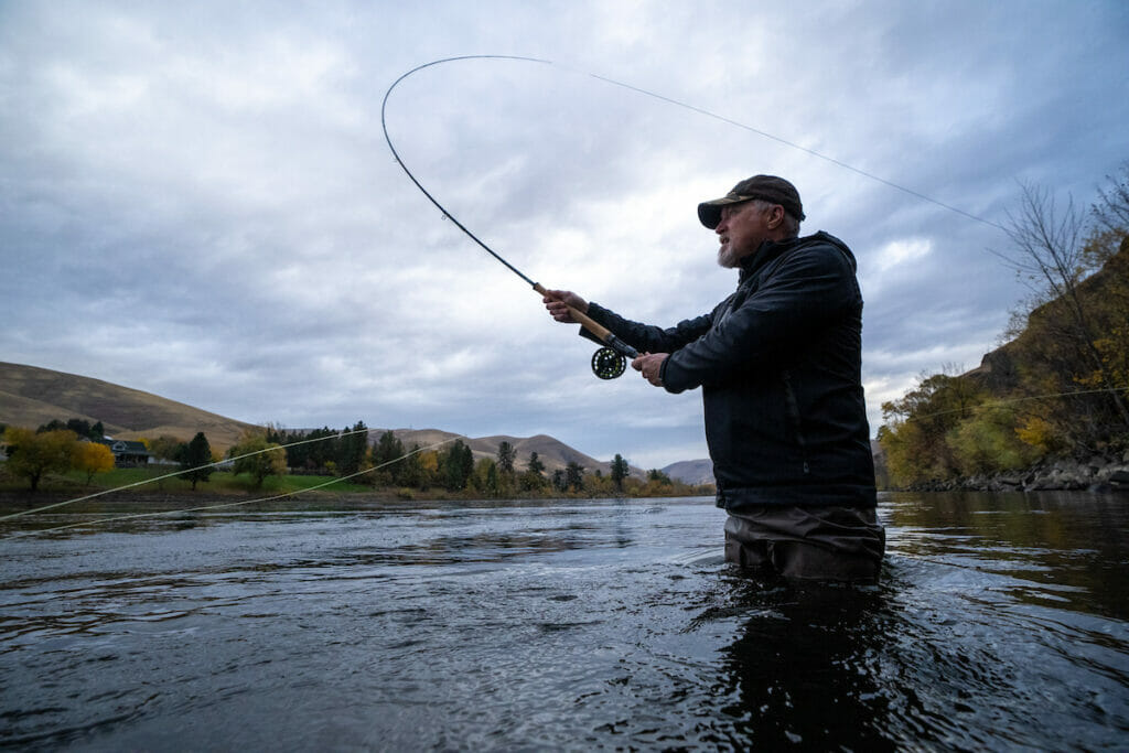 Older man in river casts back and forth