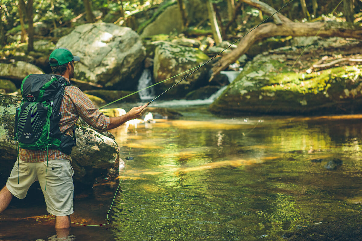 Man with backpack fly fishing in river