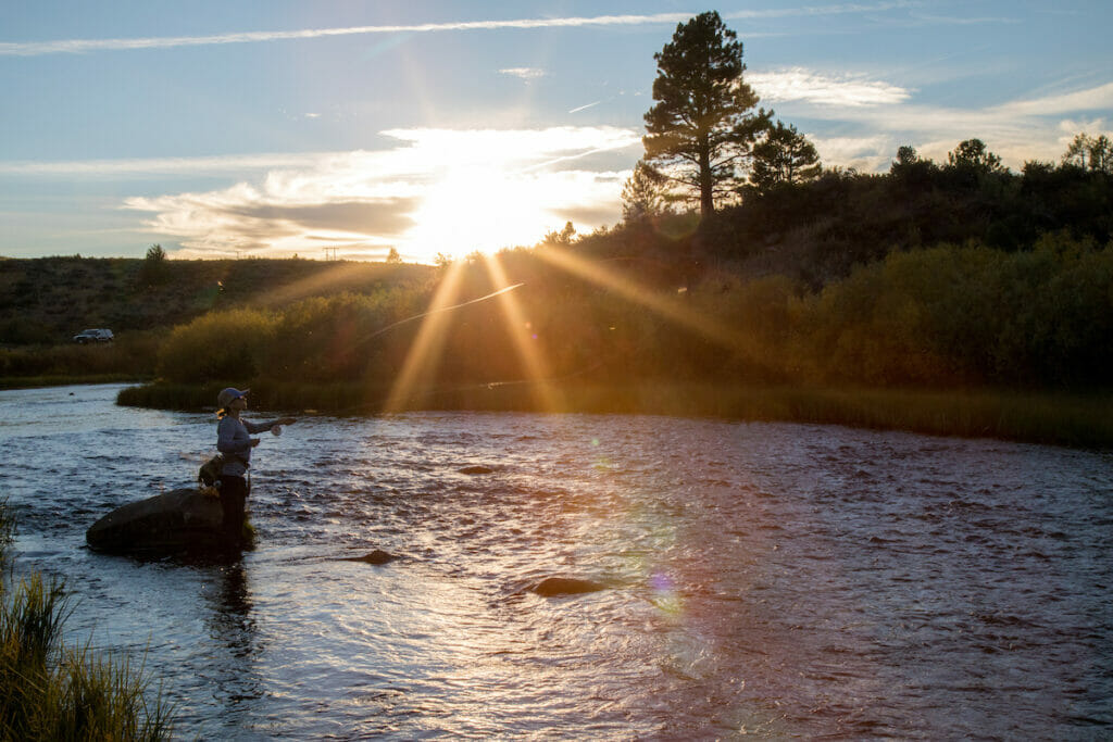 Woman casts across stream as sun sets, making good practice
