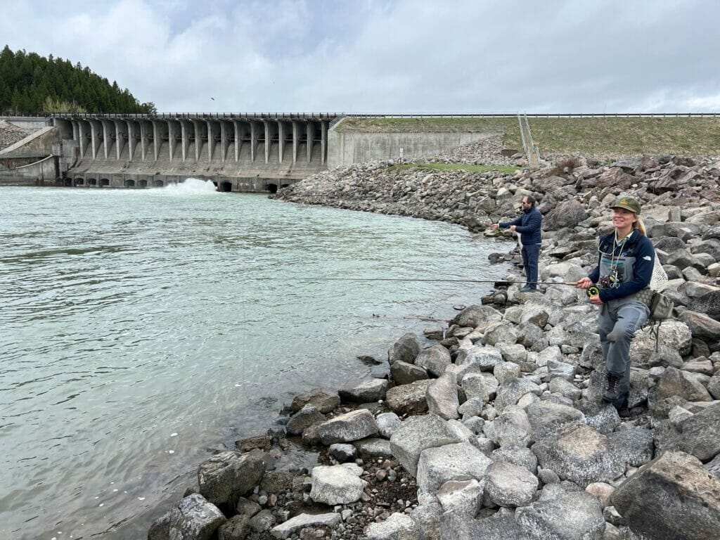 Man and woman stand on rocks fishing next to the Jackson Lake Dam