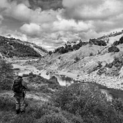 Black and white photo of man with a rod looking at a river