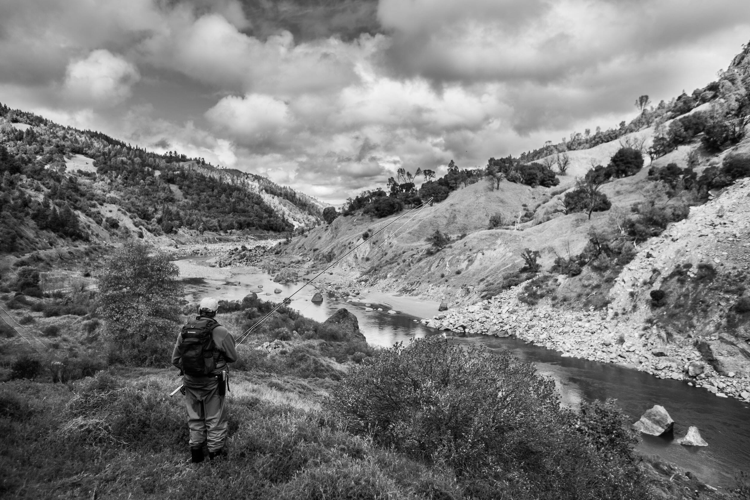 Black and white photo of man with a rod looking at a river