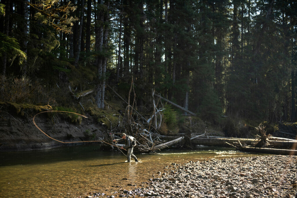 Man stands in shallow stream making a long cast