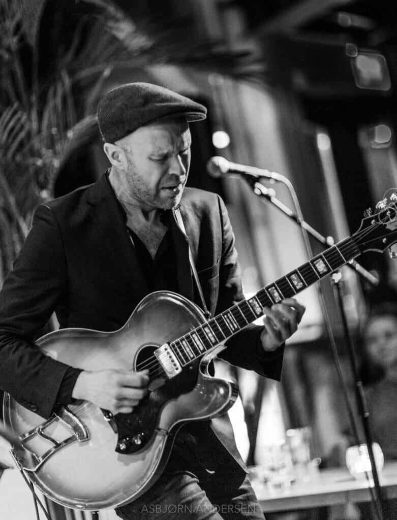 Black and white photo of man on stage playing guitar