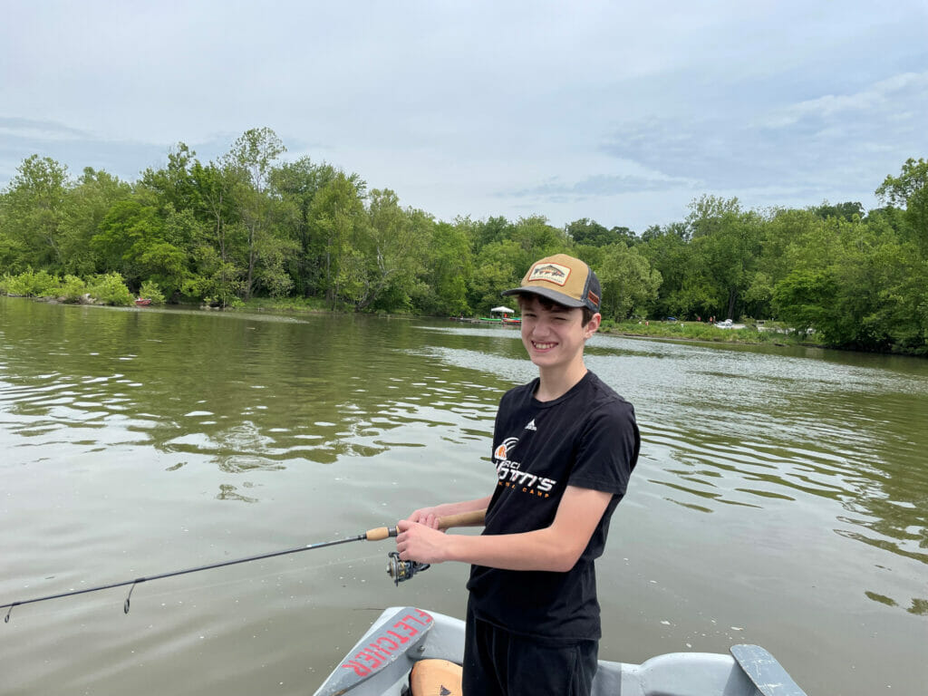 Teenage boy stands in boat, holding rod