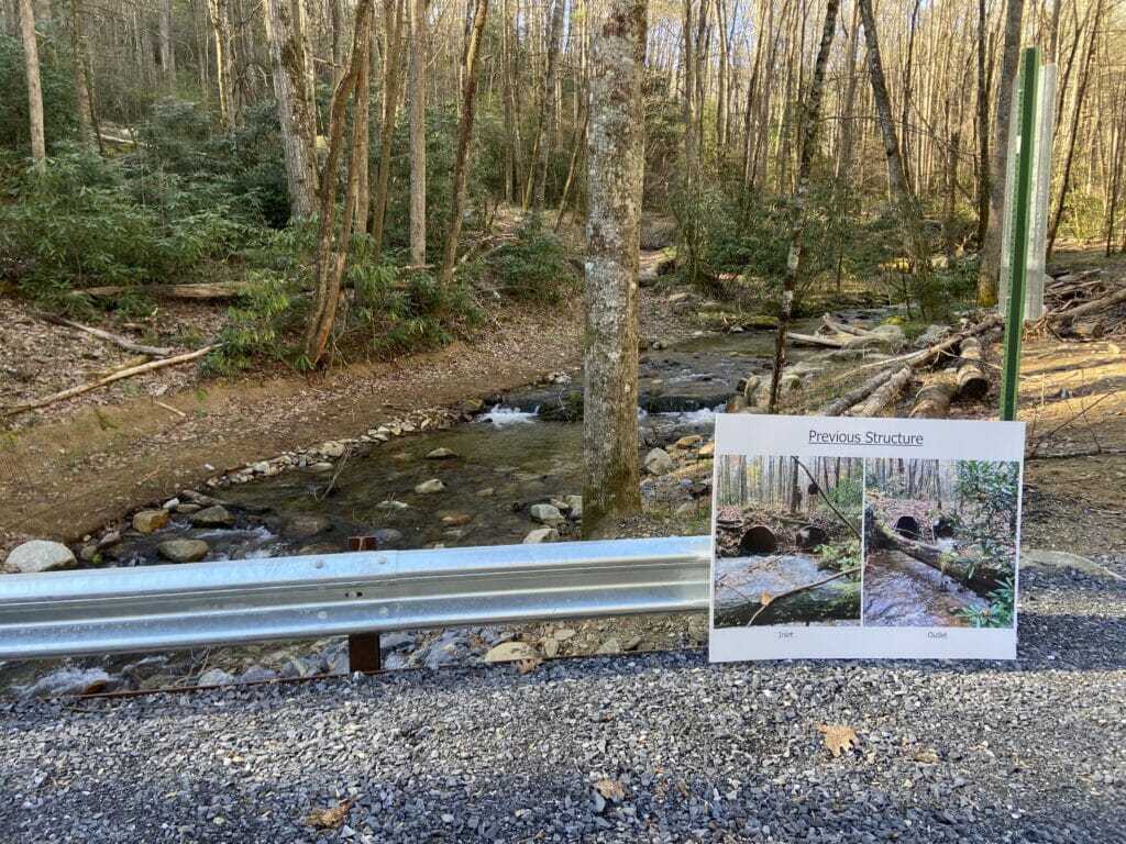 Poster leans against new bridge reading "Previous Structure" showing two culverts