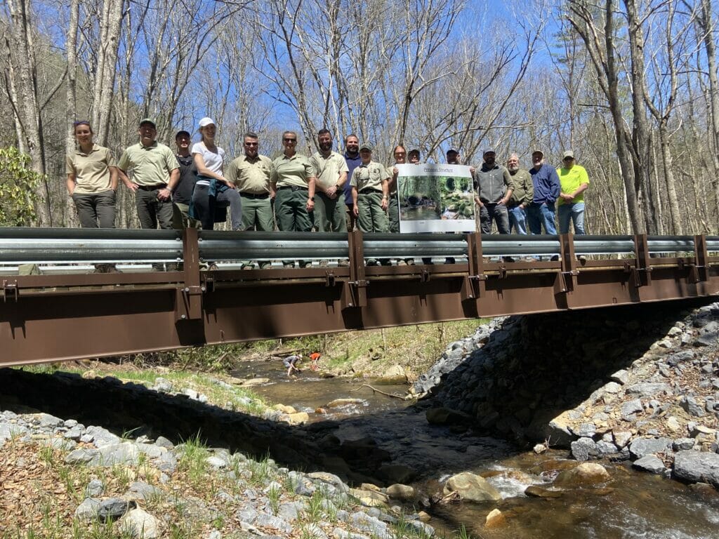 16 people stand on new bridge looking proudly at camera