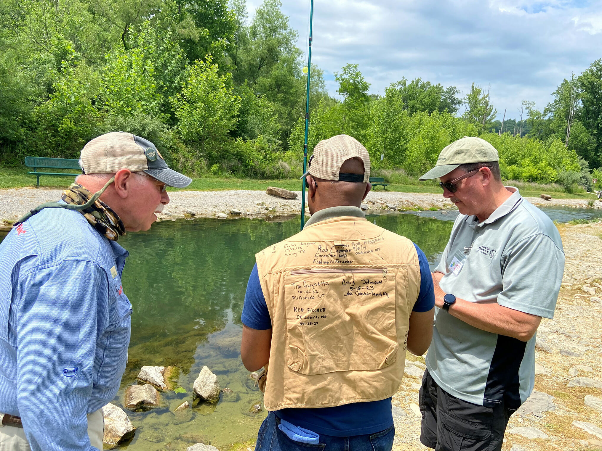 Three men stand by a river looking at the same thing