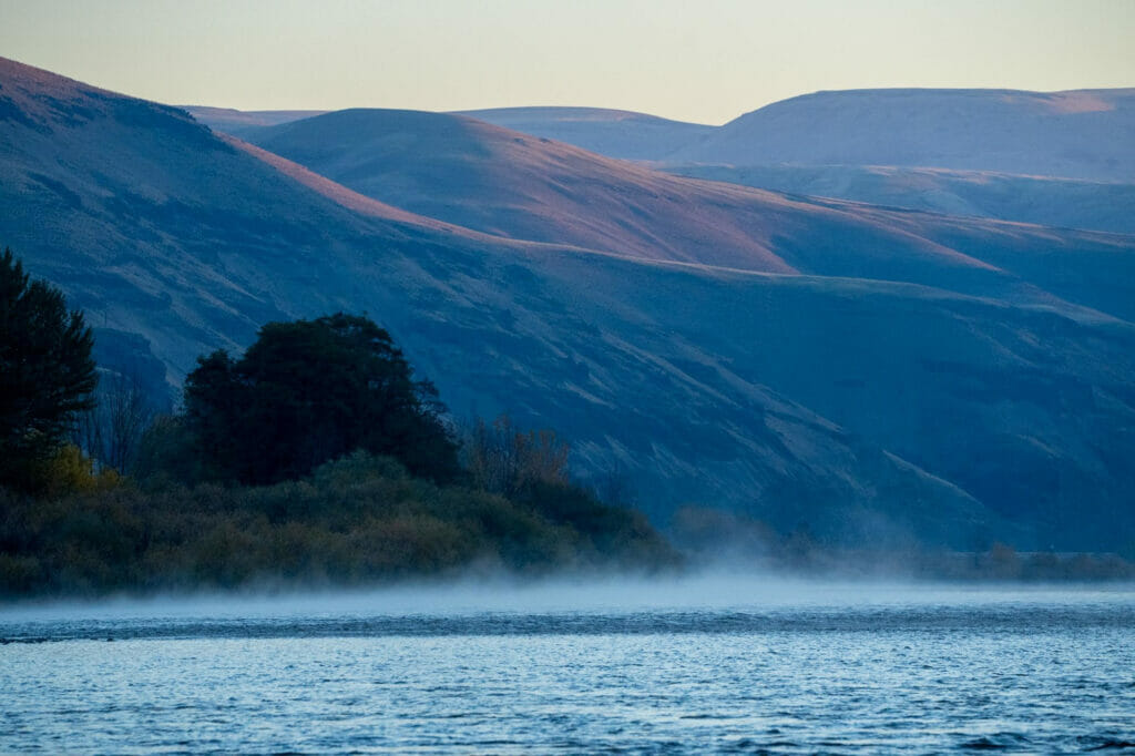 Fog on a river with sunrise mountains in the background