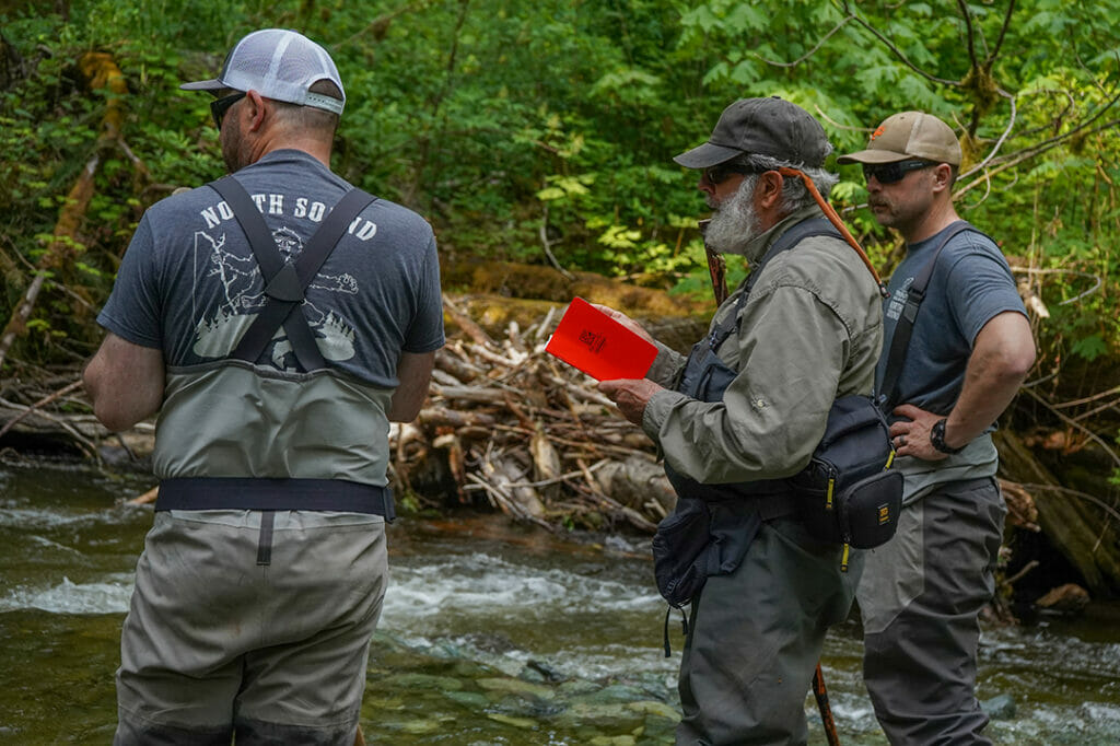 Three rugged men stand in a river recording data