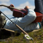 Man lays on back playing guitar with rod in the foreground