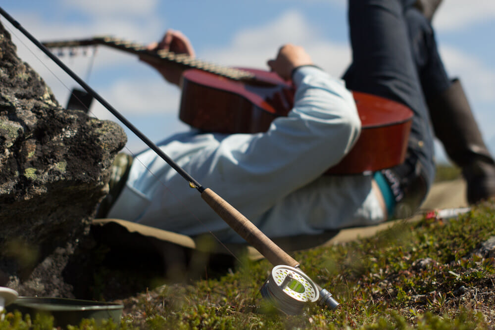 Man lays on back playing guitar with rod in the foreground