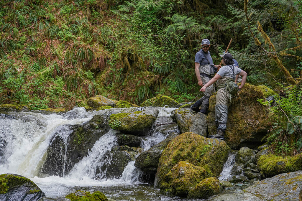 Three standing men point at rushing water