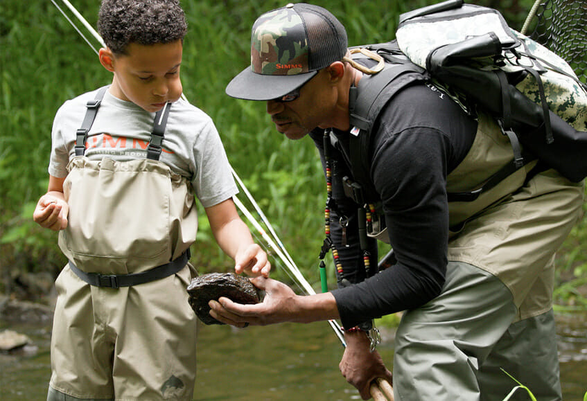 Scot Simmons hows rock to his son in a river