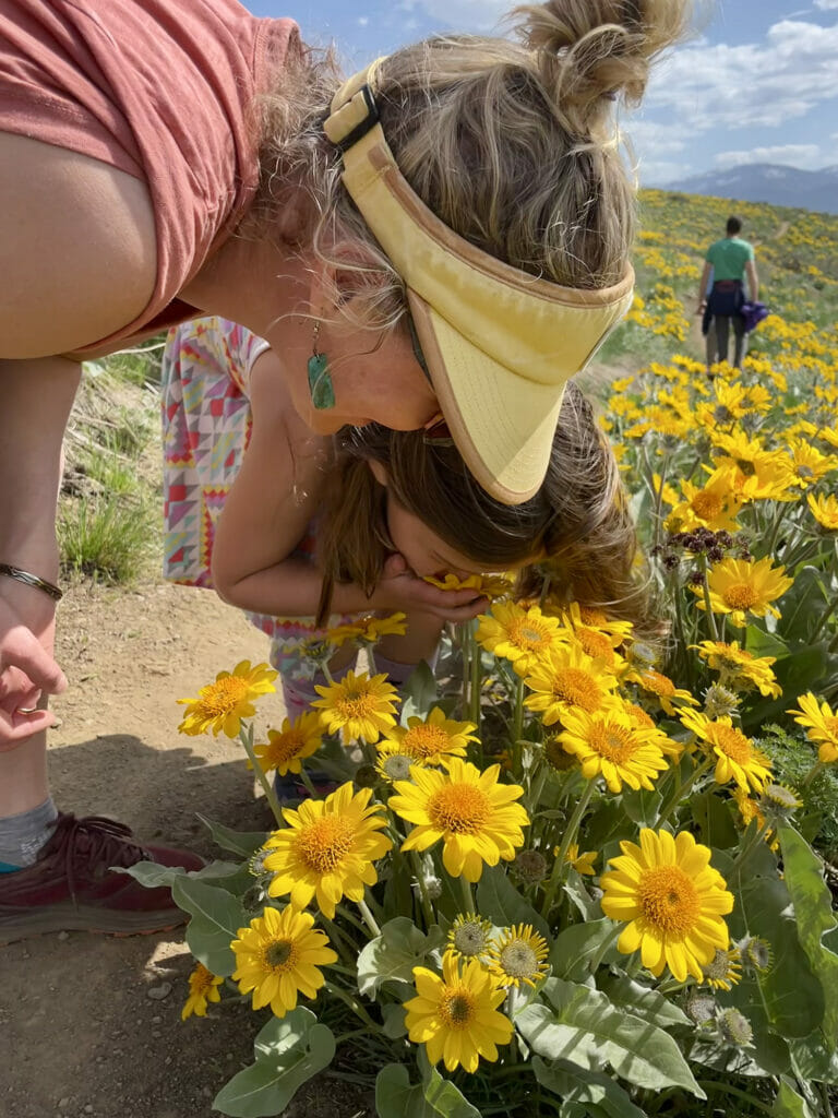 Girl and woman wearing visor bend over smelling yellow flowers