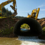 View into culvert as two back hoes dig dirt around it