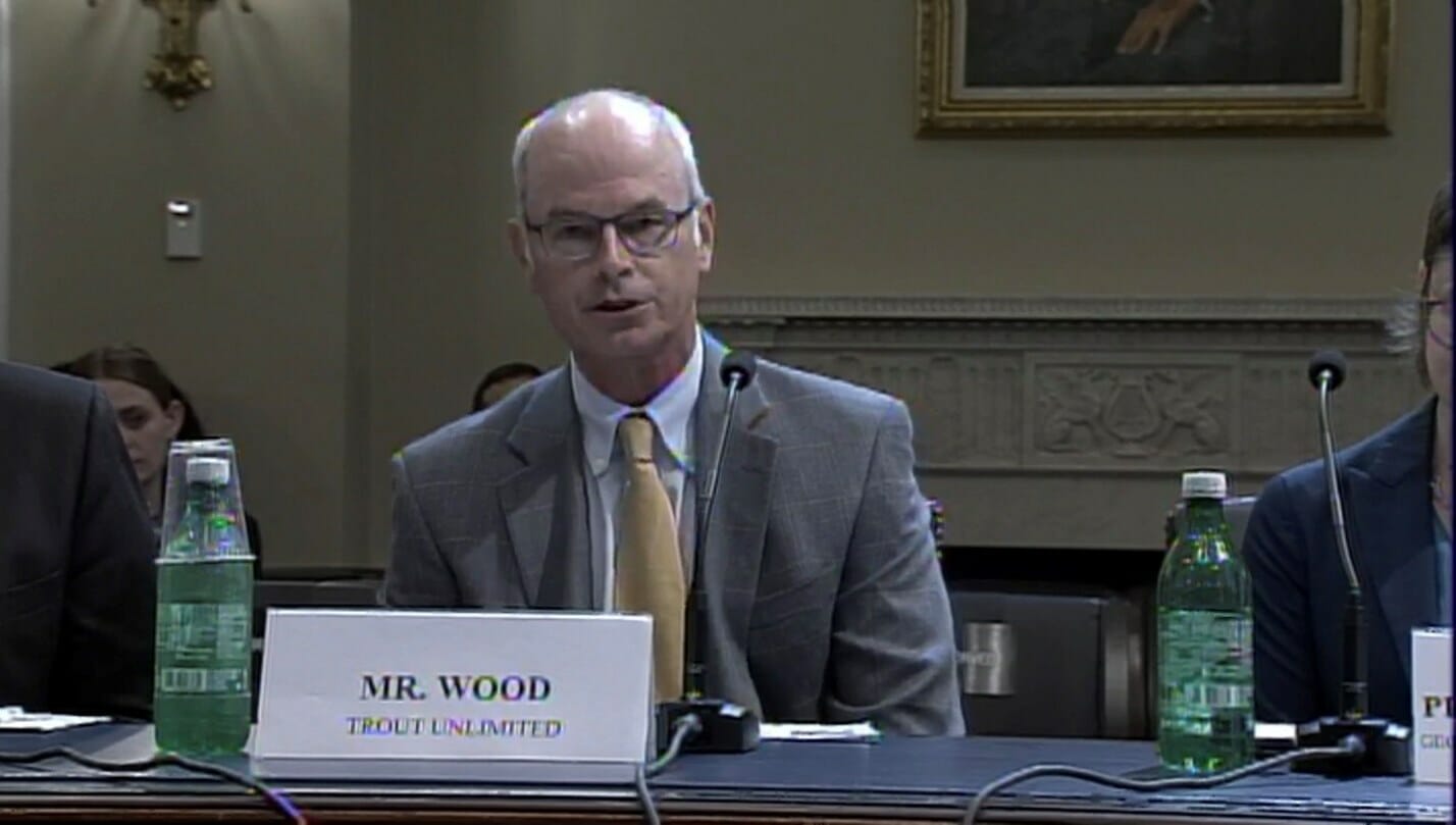 Chris Wood sits at a table speaking into a microphone